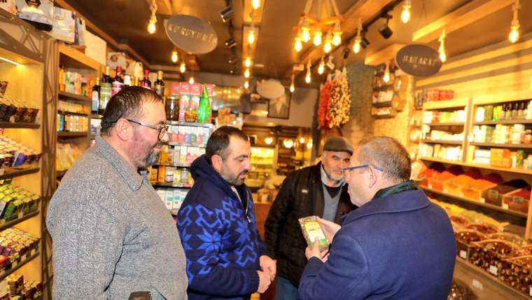 Market dükkânında rafların önünde duran dört erkekten biri elindeki ürünü diğerlerine gösteriyor.