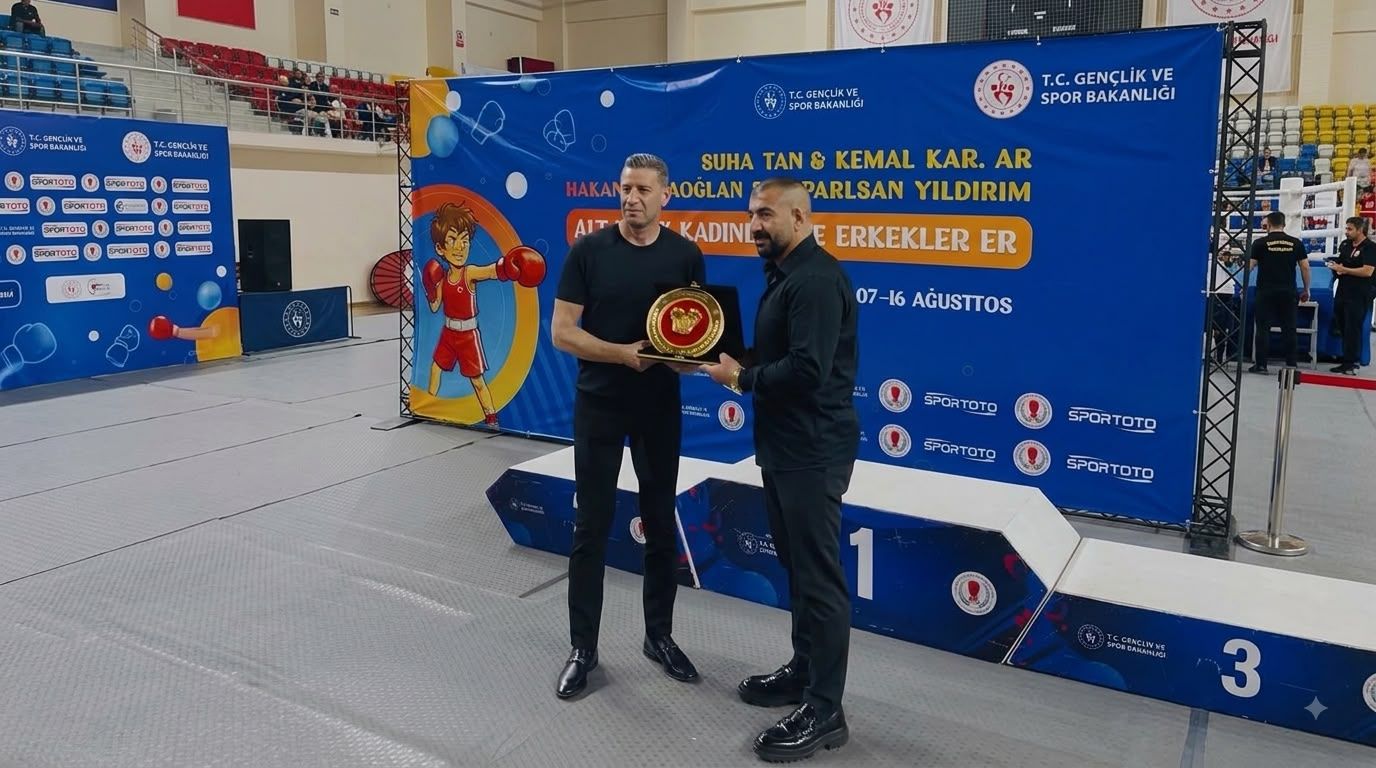 Spor salonunda iki erkek, üzerinde madalya bulunan bir kupayı tutarak boks turnuvası kürsüsünün önünde duruyor.