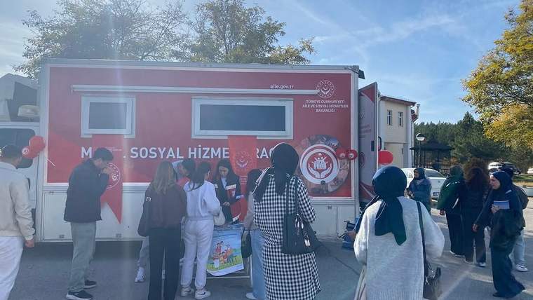Üzerinde "Mobil Sosyal Hizmet Aracı" yazılı bir araç, üniversite kampüsünde öğrencilerin etrafında duruyor.