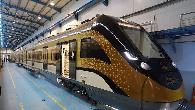 Bakım hangarında duran siyah, altın ve beyaz renkli banliyö treni; ön kapısı ve bir vagon kapısı açık.