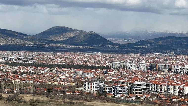 Dağların önünde, çok katlı binaların ve kırmızı çatılı evlerin yoğunlaştığı geniş bir kent manzarası