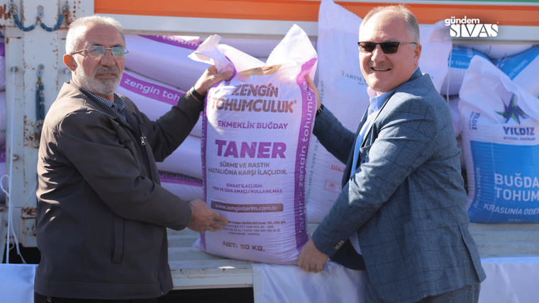 İki kişi, üzerinde 'Taner' yazılı ekmeklik buğday tohumu torbasını tutuyor.