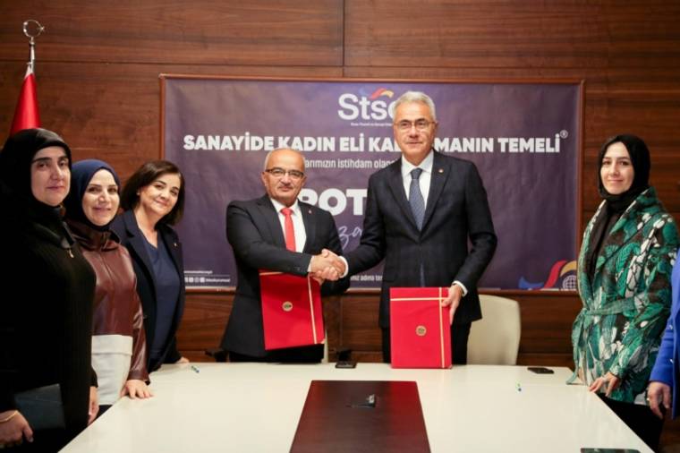 Bir masa etrafında toplanmış altı kadın ve iki erkek, belgeleri el sıkışarak takdim ediyor.