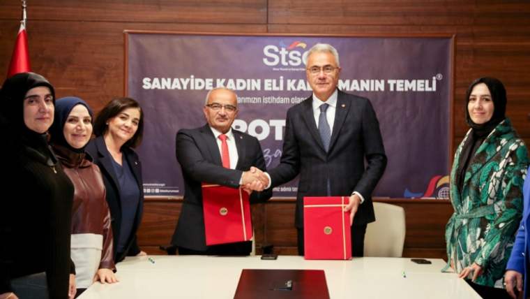 Bir masa etrafında toplanmış altı kadın ve iki erkek, belgeleri el sıkışarak takdim ediyor.