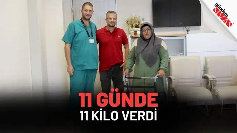İç mekânda, iki erkek ve başörtülü bir kadın; kadın yürüteç tutarken yan yana duruyor.