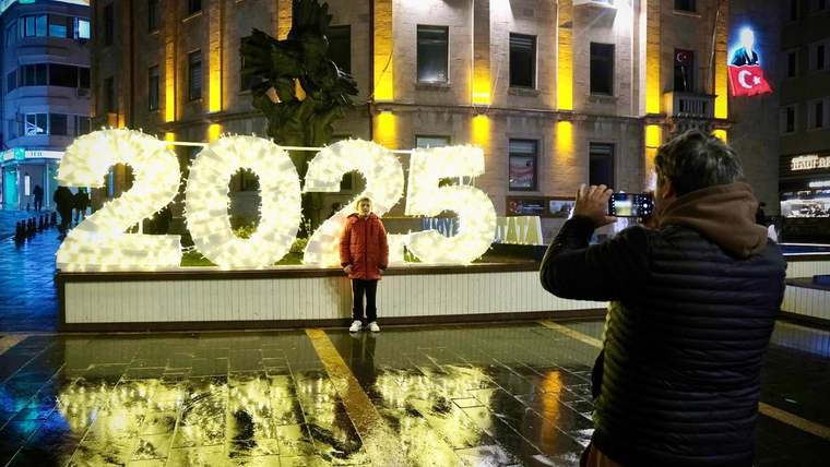 Işıklarla süslenmiş 2025 rakamlarının önünde bir kişi fotoğraf çektiriyor.