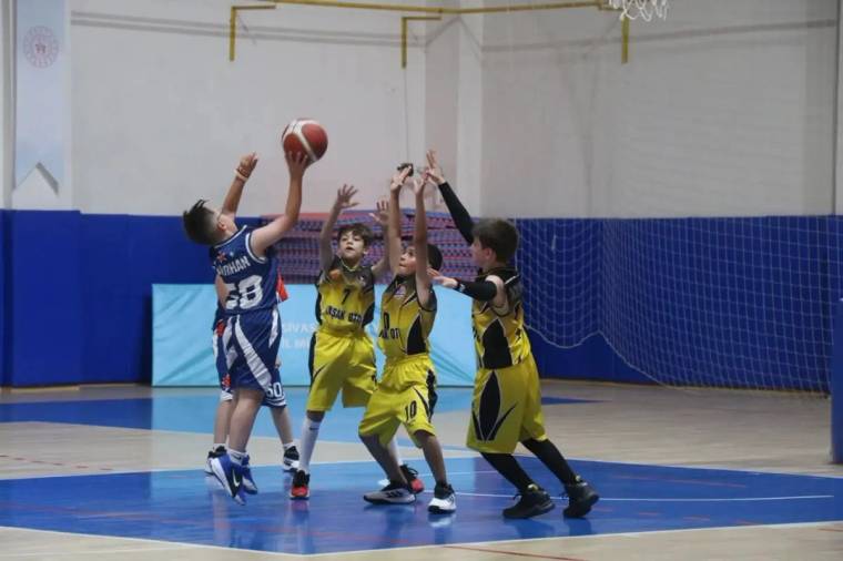 Kapalı spor salonunda çocuk basketbolcular, potaya atış yapan oyuncunun önünde savunma yapıyor.