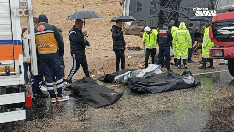 Kaza alanında, otobüsün etrafında çalışan sağlık ve güvenlik ekipleri, yağmurlu havada görev yapıyor.