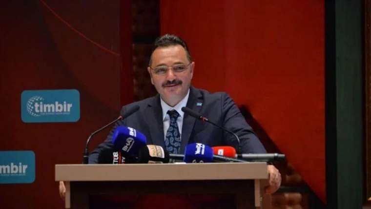 Kürsüde konuşan bir kişi, mikrofonların önünde yer alıyor.