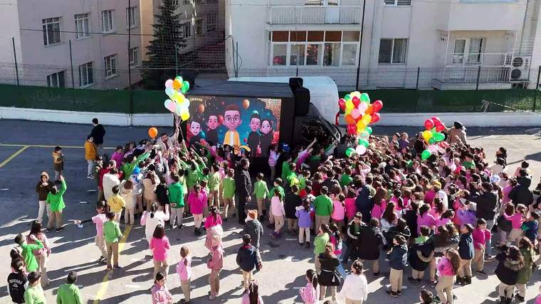 Çocuklar, açık alanda renkli balonlar tutarak etkinlikte yer alıyorlar.