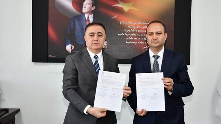 İki erkek, arkalarında Türk ve Azerbaycan bayraklarının bulunduğu panonun önünde belgeleri tutuyor.
