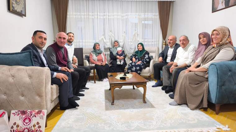 Bir oturma odasında 4 kuşak aile üyeleri bir arada oturuyor, bazıları gülümsüyor.