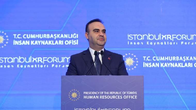 Mikrofonun önünde konuşan bir kişi, arka planda mavi bir ekran var.