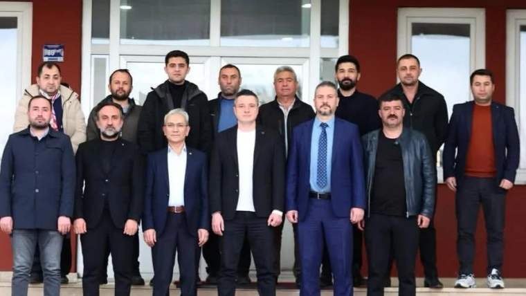 Bir binanın girişinde, takım elbiseli ve günlük giyimli yaklaşık 15 kişi birlikte duruyor.