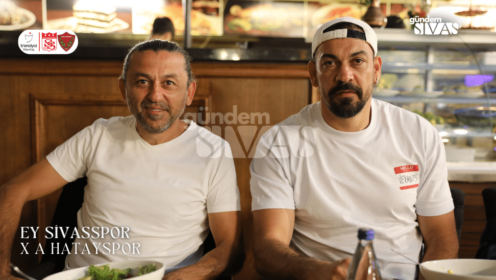 İki kişi, bir restoranda yemek yerken gülümseyerek kameraya bakıyor.