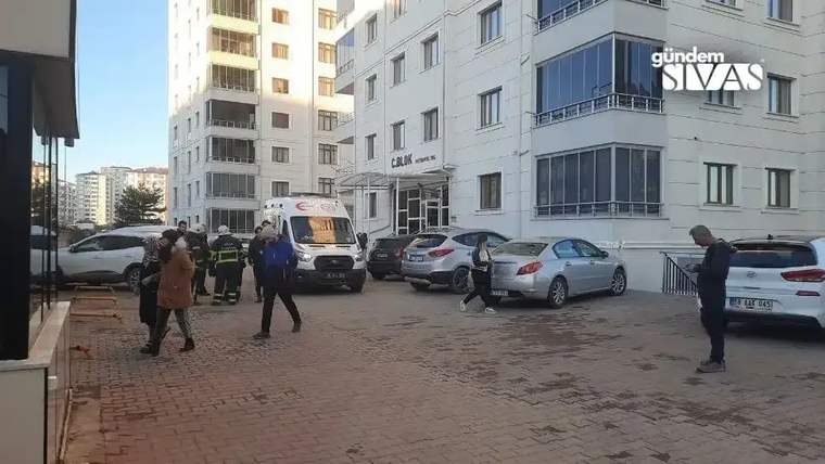 Bir grup insan, bir binanın önünde toplanmış; ambulans ve itfaiye araçları park etmiş.