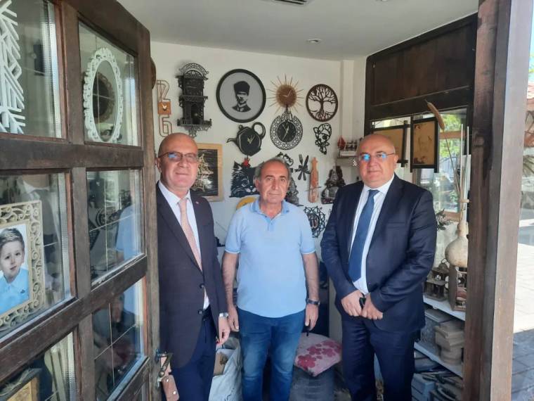 El işi süslemelerle çevrili dükkânda, kapı eşiğinde yan yana duran üç kişi görülüyor.