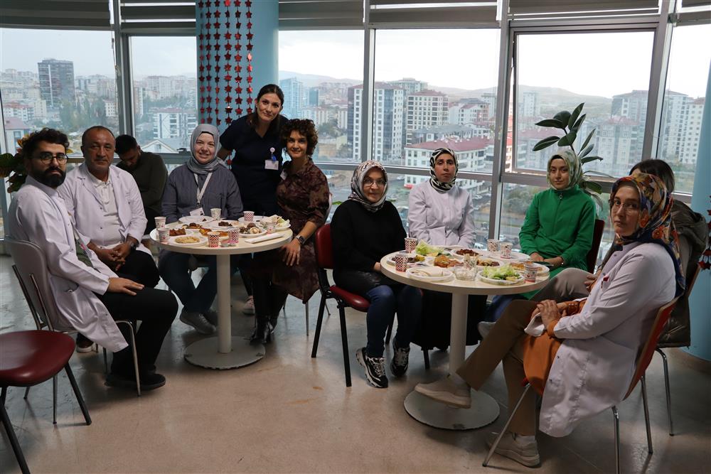 Bir grup sağlık çalışanı ve hasta, yuvarlak masada yemek yerken gülümseyerek poz veriyor.