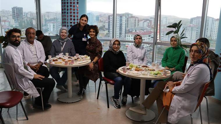Bir grup sağlık çalışanı ve hasta, yuvarlak masada yemek yerken gülümseyerek poz veriyor.