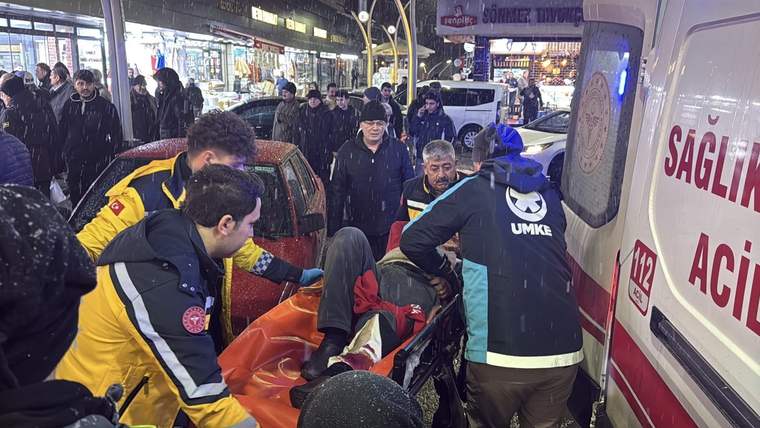 Ambulansa taşınan yaralı bir kişi, etrafında sağlık ekipleri ve kalabalık var.