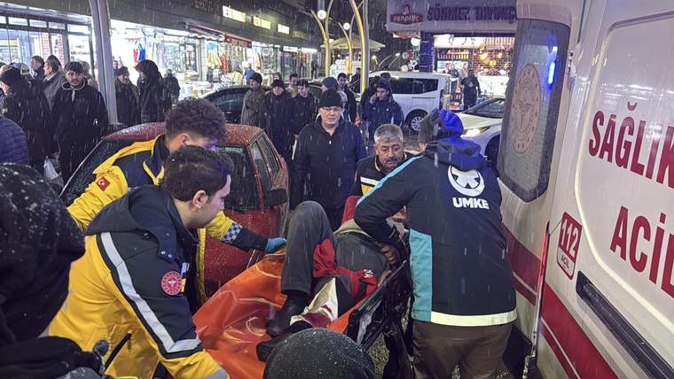 Ambulansa taşınan yaralı bir kişi, etrafında sağlık ekipleri ve kalabalık var.