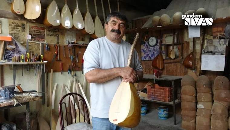 Bir adam, elinde bir bağlama tutarak atölyede duruyor. Arka planda çeşitli müzik aletleri ve aletlerin yapımında kullanılan malzemeler yer alıyor.