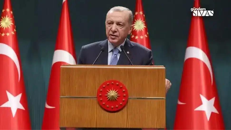 Kürsüde konuşan bir kişi, arkasında Türk bayraklarıyla birlikte duruyor.