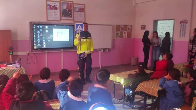 Sınıfta oturan ilkokul öğrencilerine, elinde yaya geçidi levhası bulunan bir görevli sunum yapıyor.