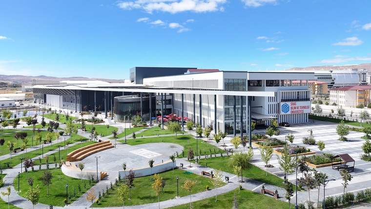 SBTÜ kampüsünde modern bir bina, çevresinde yeşil alanlar ve ağaçlar yer alıyor.