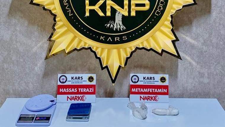 Üzerinde Kars ve NARKO yazan kartların önünde iki hassas terazi ile poşetlenmiş maddeler bulunuyor.