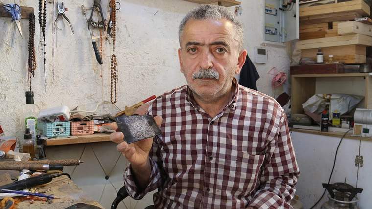 Kareli gömlek giymiş bir adam, elinde kemik tarağı tutuyor ve gülümseyerek kameraya bakıyor.