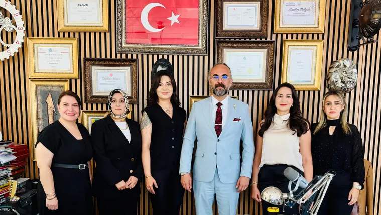 Bir grup insan, arka planda Türk bayrağı ve çeşitli sertifikalarla birlikte poz veriyor.