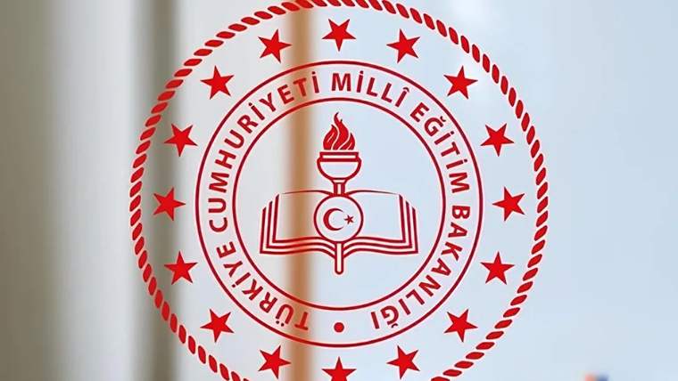 Duvar ve masa üzerinde, Türkiye Cumhuriyeti Millî Eğitim Bakanlığı amblemi bulunan bir sınıf veya ofis ortamı.