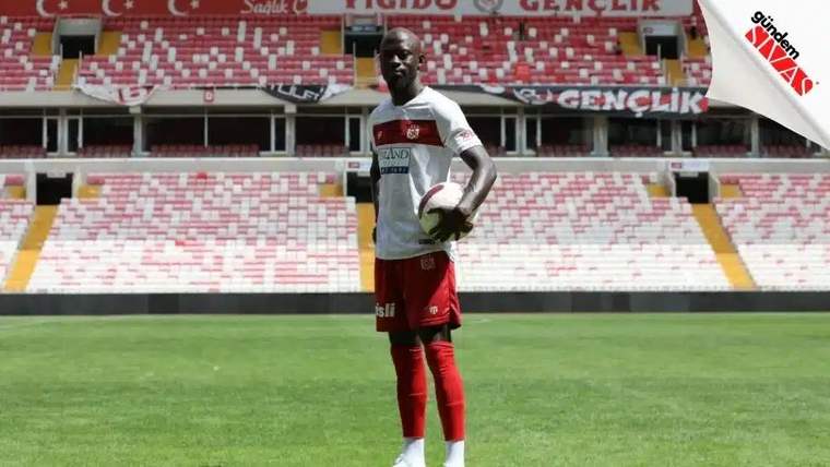 Sivasspor forması giymiş bir futbolcu, stadyumda top tutarak poz veriyor.