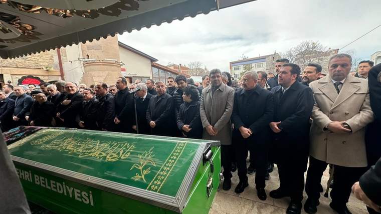 Bir grup insan, yeşil bir tabutun etrafında toplanmış, cenaze törenine katılıyor.