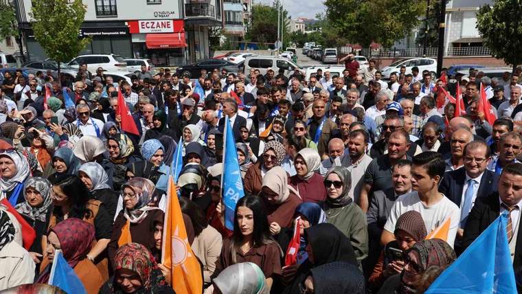 Sokakta toplanan kalabalık arasında farklı renklerde bayraklar taşınıyor; arka planda “Eczane” tabelası görülüyor.