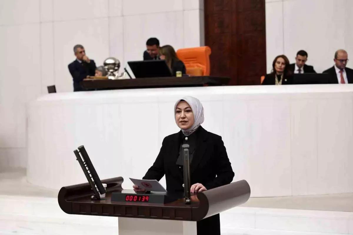 Beyaz başörtülü bir kadın, arkasında oturan kişiler ve elektronik sayaç bulunan kürsüde konuşuyor.