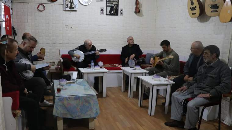 Masalar çevresinde oturan kişilerden bazıları bağlama ve gitar çalarken, duvarlarda çeşitli çalgılar asılı duruyor.
