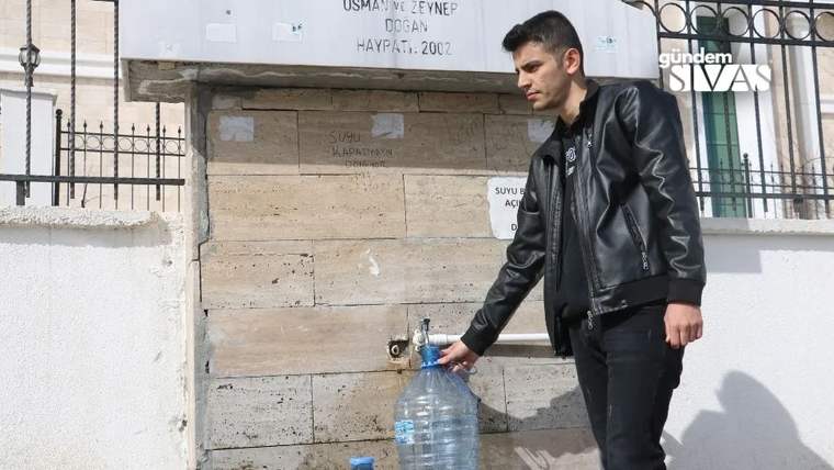 Bir genç, çeşmeden su doldurmak için su şişesini tutuyor.