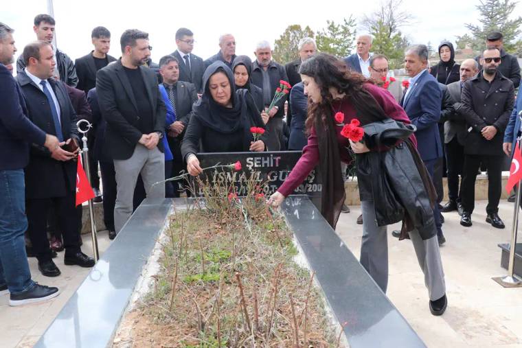 Bir grup insan, mezar başında çiçek bırakıyor; arka planda Türk bayrakları var.