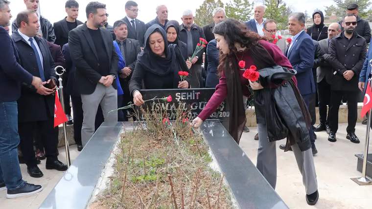 Bir grup insan, mezar başında çiçek bırakıyor; arka planda Türk bayrakları var.