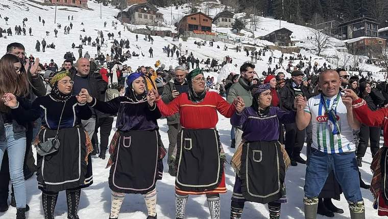 Kar kaplı alanda geleneksel kıyafetli dört kişi el ele dururken çevrelerinde kalabalık izliyor.