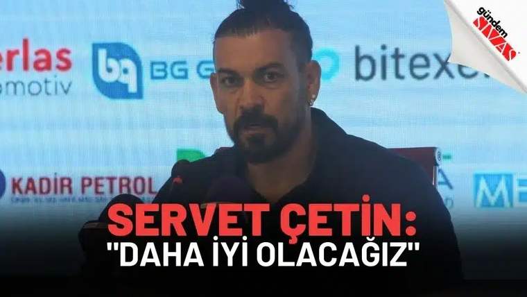 Bir basın toplantısında konuşan bir kişi, mikrofonların önünde yer alıyor.