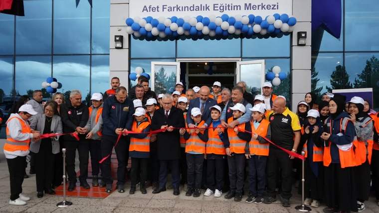 Afet Farkındalık Eğitim Merkezi'nin açılışında kurdele kesen kalabalık, turuncu yelek giymiş kişilerle birlikte poz veriyor.