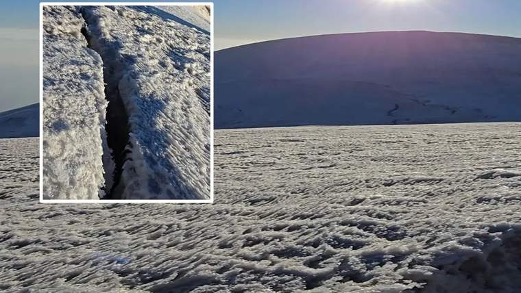 Güneş altında karla kaplı dağ yamacı ve karda uzanan derin bir yarık görülüyor.