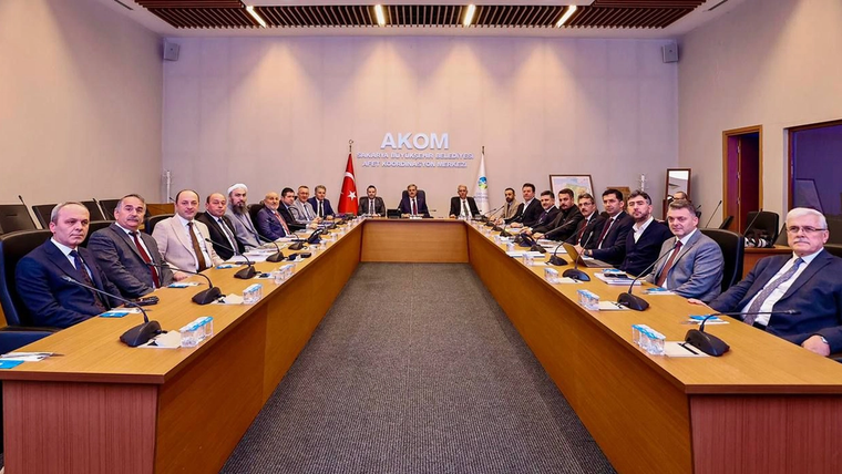 AKOM yazılı toplantı salonunda, U biçimli masanın çevresinde çok sayıda kişi oturuyor; Türk bayrağı görülüyor.