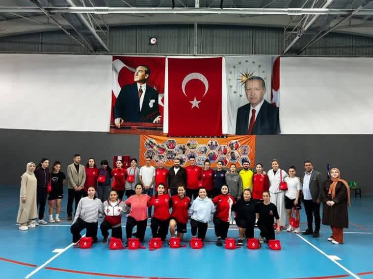 Spor salonunda, Türk bayrakları ve portreler önünde kırmızı eşofmanlı kalabalık grup poz veriyor.