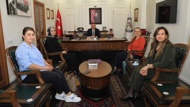 Bir masa etrafında oturan beş kadın, arka planda bir erkek oturuyor.