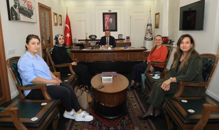 Bir masa etrafında oturan beş kadın, arka planda bir erkek oturuyor.