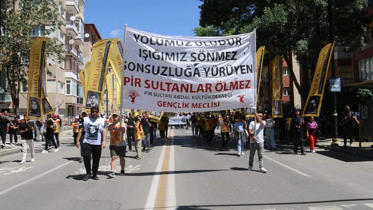 Büyük bir pankart taşıyan kalabalık, sokakta yürüyüş yapıyor.